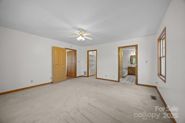 unfurnished bedroom with ceiling fan, light colored carpet, a spacious closet, connected bathroom, and a closet