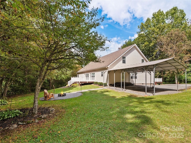 back of house with a lawn, an outdoor fire pit, a deck, and a carport