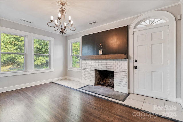 unfurnished living room featuring a healthy amount of sunlight, wood-type flooring, an inviting chandelier, and a brick fireplace