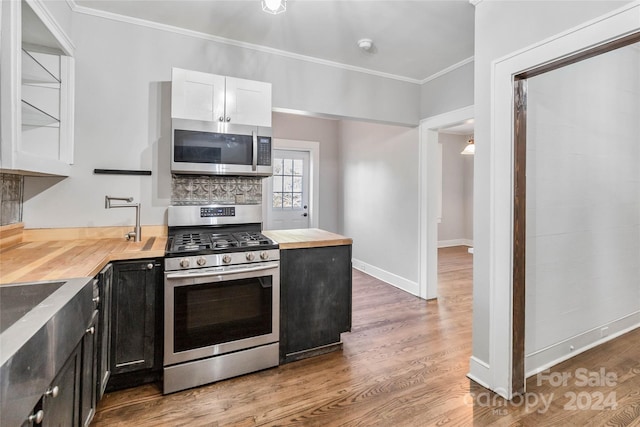 kitchen featuring ornamental molding, butcher block countertops, white cabinetry, appliances with stainless steel finishes, and hardwood / wood-style floors