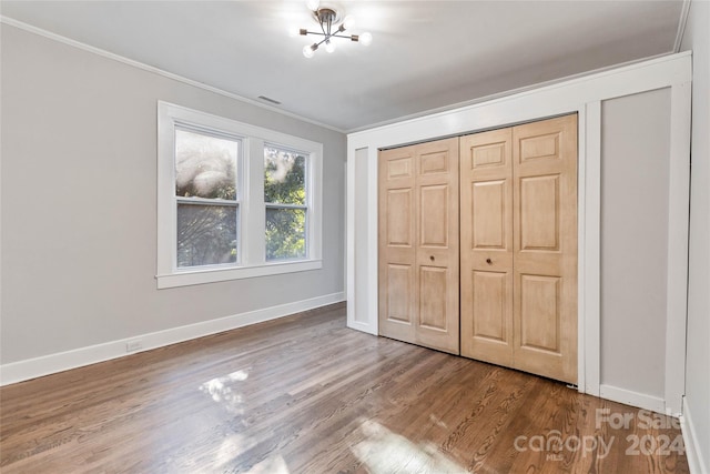 unfurnished bedroom with ornamental molding, hardwood / wood-style floors, a chandelier, and a closet