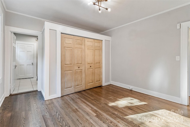 unfurnished bedroom with wood-type flooring, ornamental molding, an inviting chandelier, and a closet