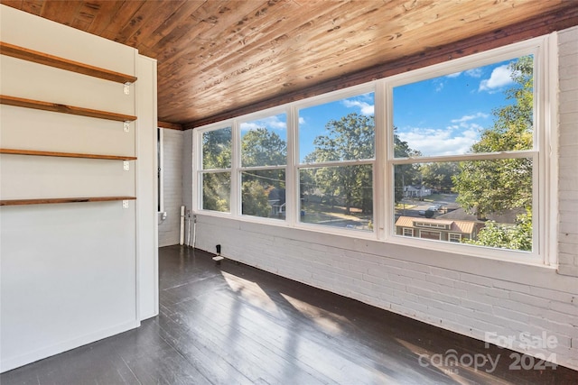 unfurnished room featuring plenty of natural light, dark hardwood / wood-style flooring, and brick wall