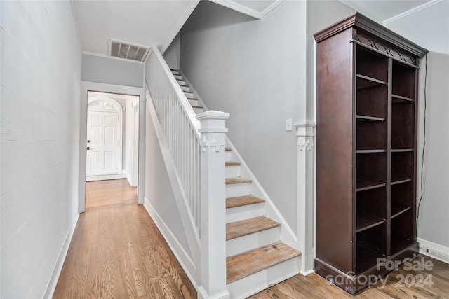 stairway with wood-type flooring and crown molding