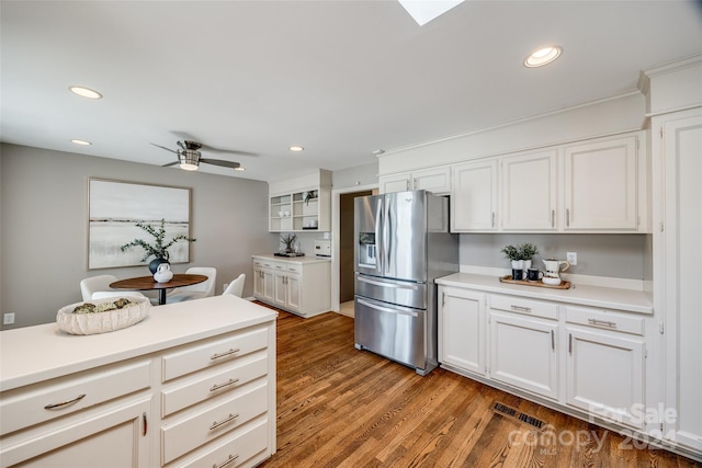 kitchen featuring stainless steel fridge, white cabinets, wood-type flooring, and ceiling fan