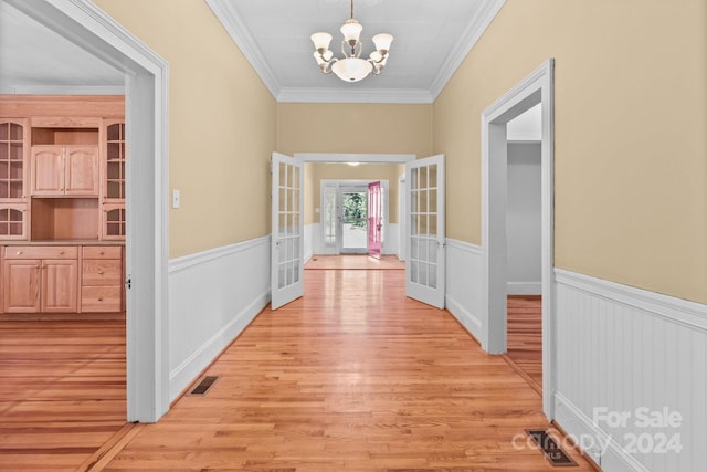 hall featuring light wood-type flooring, crown molding, french doors, and a notable chandelier