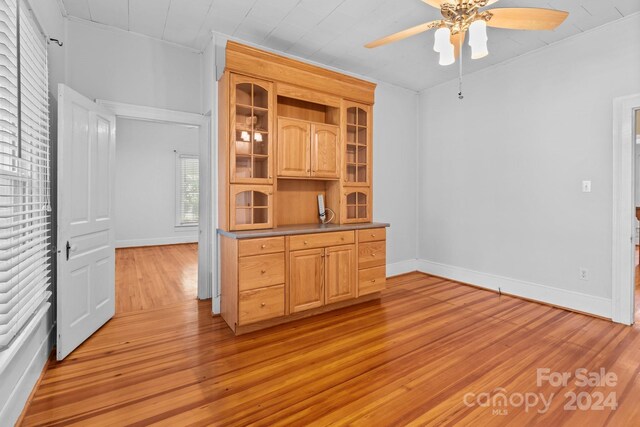 bar featuring ceiling fan, light brown cabinets, light wood-type flooring, and crown molding