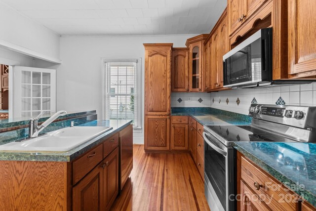 kitchen featuring stainless steel range with electric cooktop, decorative backsplash, light hardwood / wood-style floors, and sink