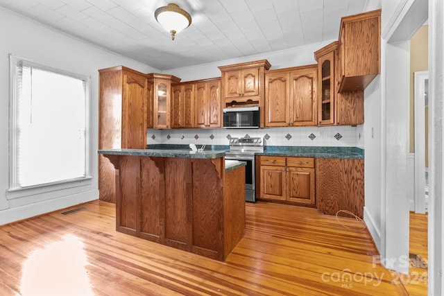 kitchen featuring appliances with stainless steel finishes, dark stone countertops, tasteful backsplash, a breakfast bar area, and light wood-type flooring