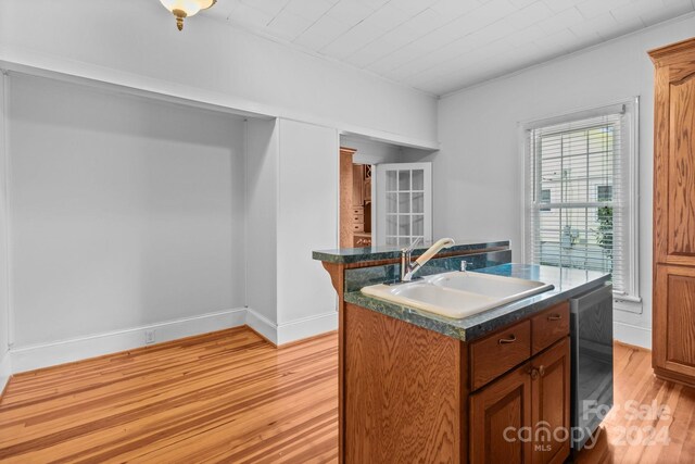 kitchen featuring an island with sink, wine cooler, light wood-type flooring, ornamental molding, and sink