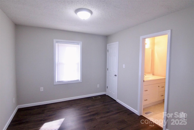 unfurnished bedroom with ensuite bath, dark wood-type flooring, a textured ceiling, and sink