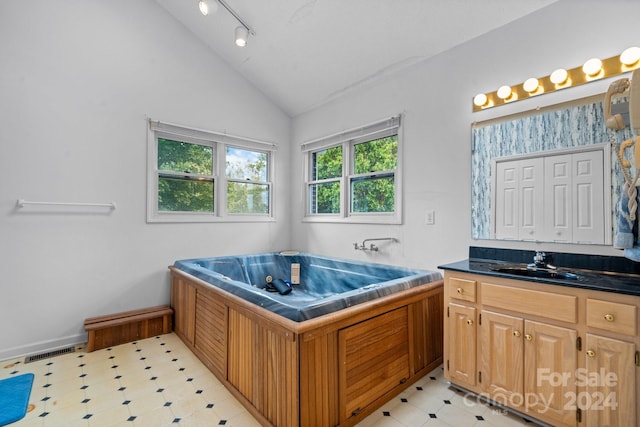 bathroom featuring vanity, track lighting, vaulted ceiling, and a bath