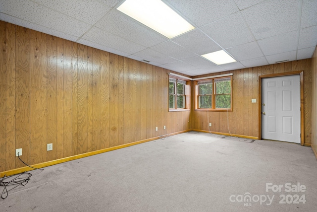 unfurnished room with carpet, a paneled ceiling, and wooden walls