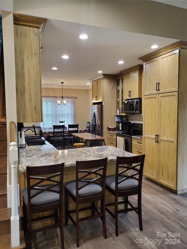 kitchen featuring a chandelier, light stone counters, hardwood / wood-style flooring, kitchen peninsula, and stainless steel appliances