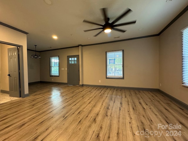 empty room featuring ceiling fan with notable chandelier, light hardwood / wood-style flooring, and a wealth of natural light