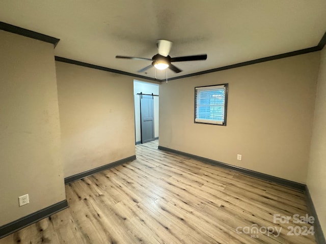 spare room with light wood-type flooring, crown molding, a barn door, and ceiling fan