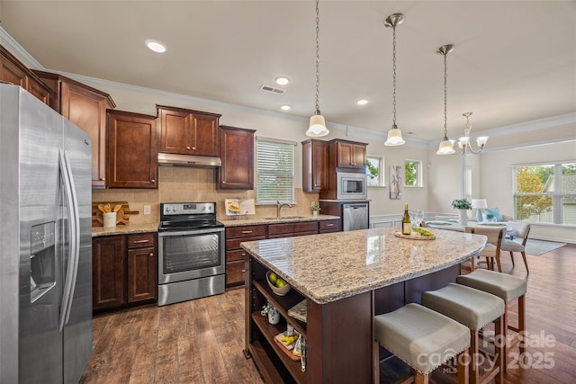 kitchen featuring under cabinet range hood, a sink, a kitchen island, dark wood finished floors, and stainless steel appliances