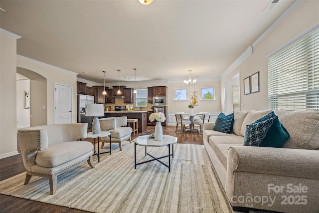 living room featuring arched walkways, visible vents, ornamental molding, and wood finished floors