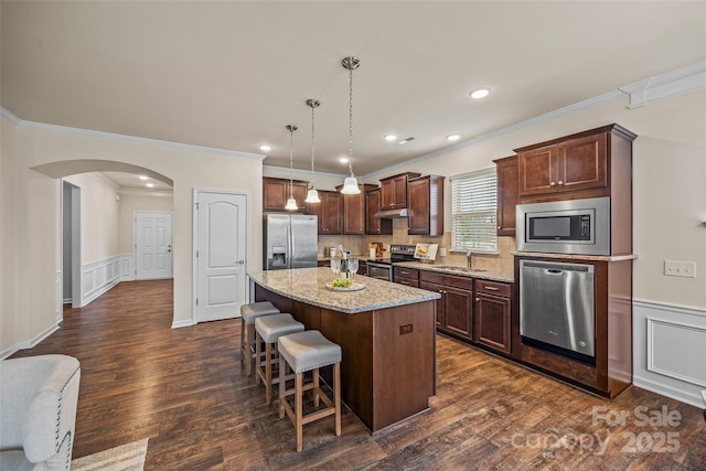 kitchen featuring a kitchen island, light stone countertops, a breakfast bar area, arched walkways, and stainless steel appliances