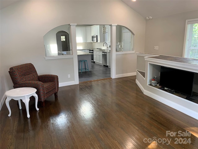sitting room with dark wood-style floors, lofted ceiling, arched walkways, and baseboards