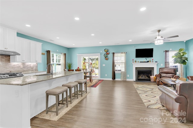 kitchen with dark stone countertops, white cabinetry, light wood-type flooring, ceiling fan, and sink