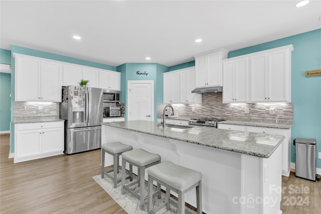 kitchen with appliances with stainless steel finishes, light hardwood / wood-style floors, white cabinetry, a kitchen island with sink, and sink