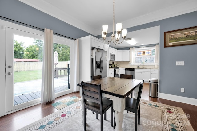 dining space with ornamental molding, a notable chandelier, sink, and dark wood-type flooring