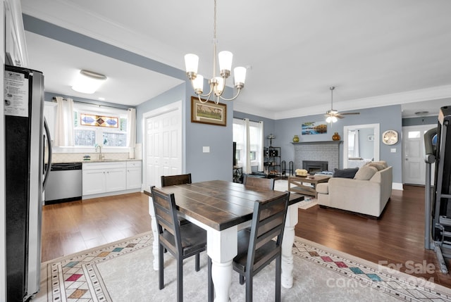 dining room featuring ceiling fan with notable chandelier, dark hardwood / wood-style flooring, sink, a fireplace, and ornamental molding