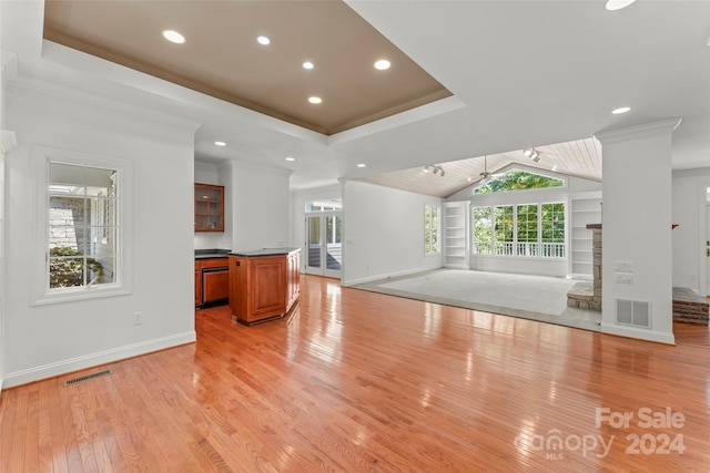 unfurnished living room with ornamental molding, light hardwood / wood-style flooring, a tray ceiling, a fireplace, and vaulted ceiling