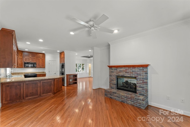 kitchen featuring ceiling fan, kitchen peninsula, a brick fireplace, light hardwood / wood-style flooring, and black appliances