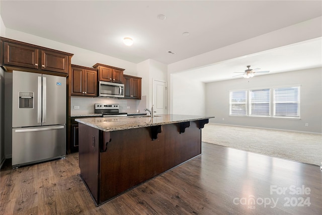 kitchen with decorative backsplash, dark wood-type flooring, a breakfast bar area, appliances with stainless steel finishes, and a center island with sink