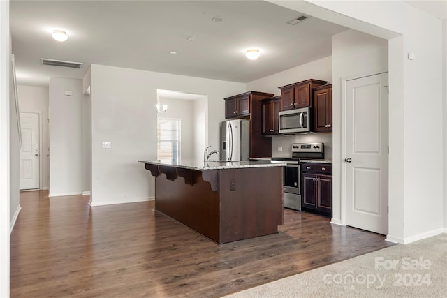 kitchen with stainless steel appliances, dark wood-type flooring, a center island with sink, dark brown cabinets, and a kitchen bar