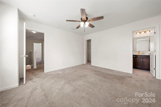 unfurnished bedroom featuring a closet, light colored carpet, ensuite bathroom, and ceiling fan