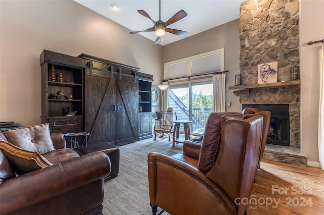 living room featuring ceiling fan, a stone fireplace, high vaulted ceiling, light wood-type flooring, and a barn door