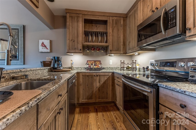 kitchen with light stone counters, stainless steel appliances, light wood-type flooring, and sink