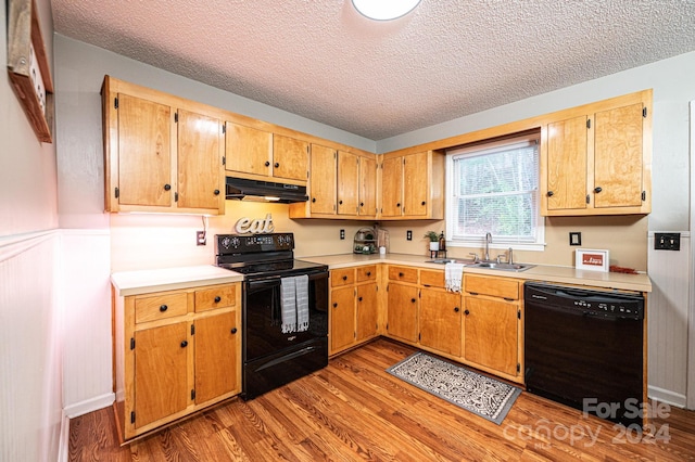 kitchen with black appliances, light wood-type flooring, sink, and a textured ceiling