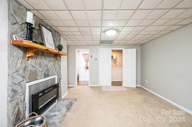 living room featuring a stone fireplace, light carpet, and a drop ceiling