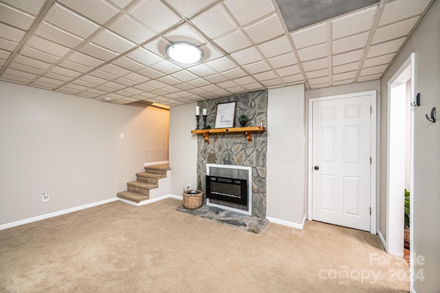 unfurnished living room featuring carpet, a paneled ceiling, and a stone fireplace