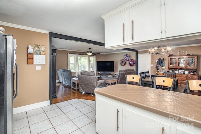 kitchen with light tile patterned floors, white cabinetry, stainless steel refrigerator, tile counters, and ceiling fan with notable chandelier