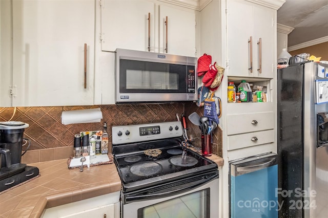 kitchen featuring ornamental molding, white cabinetry, appliances with stainless steel finishes, tile countertops, and decorative backsplash