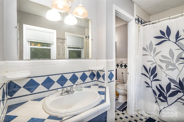 bathroom with tile walls, a textured ceiling, a shower with shower curtain, vanity, and toilet