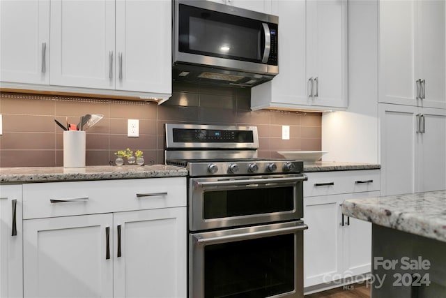 kitchen with white cabinets, appliances with stainless steel finishes, backsplash, and light stone countertops