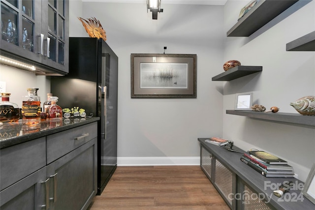 bar featuring dark stone counters, black refrigerator, and dark hardwood / wood-style flooring