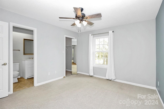 unfurnished bedroom featuring a closet, ceiling fan, a walk in closet, ensuite bathroom, and light colored carpet