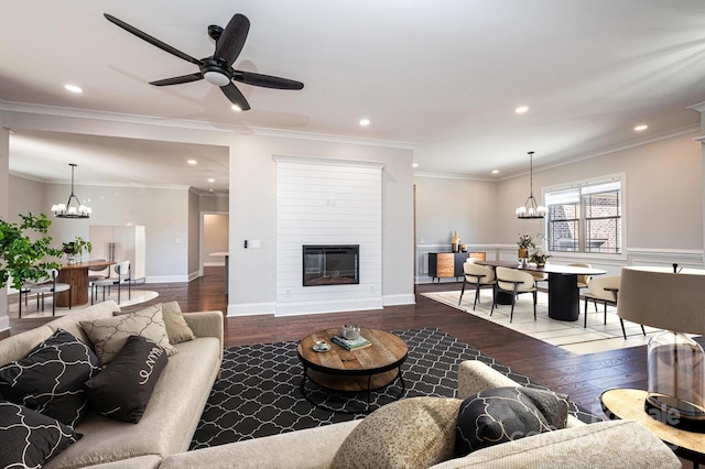 living area featuring a large fireplace, hardwood / wood-style flooring, ornamental molding, ceiling fan with notable chandelier, and recessed lighting