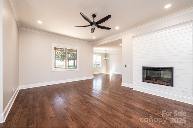 unfurnished living room with dark wood-type flooring, a large fireplace, ornamental molding, and ceiling fan with notable chandelier