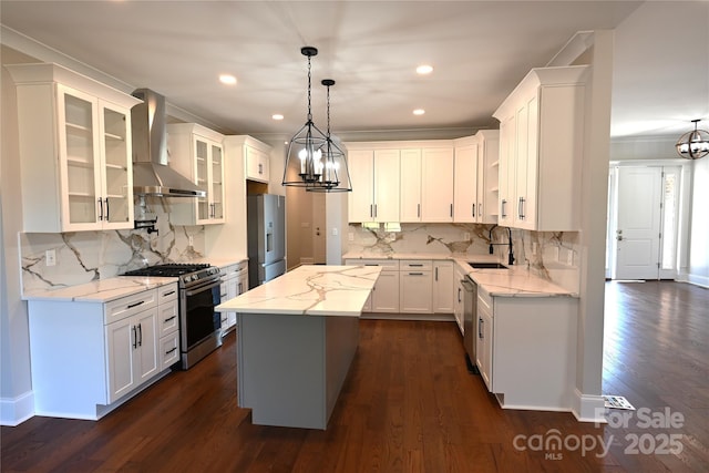 kitchen with appliances with stainless steel finishes, white cabinets, a kitchen island, wall chimney range hood, and a sink