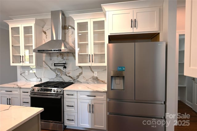 kitchen with wall chimney exhaust hood, appliances with stainless steel finishes, glass insert cabinets, and white cabinets