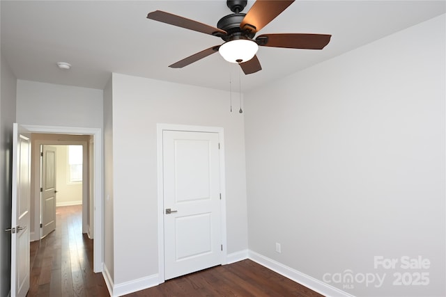 unfurnished bedroom with dark wood-type flooring, a ceiling fan, and baseboards