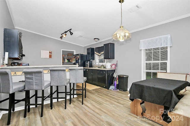 kitchen featuring light wood-type flooring, a textured ceiling, vaulted ceiling, a kitchen bar, and crown molding